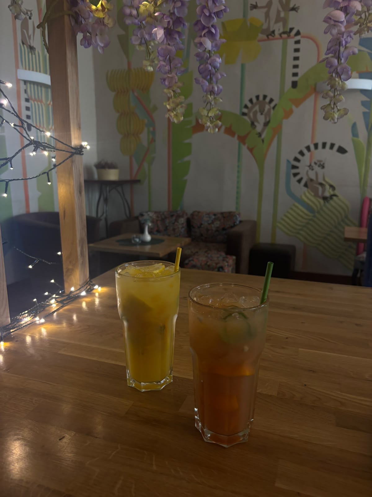 Two tall glasses of homemade lemonade on a sunlit table, fairy lights and painted jungle wall behind