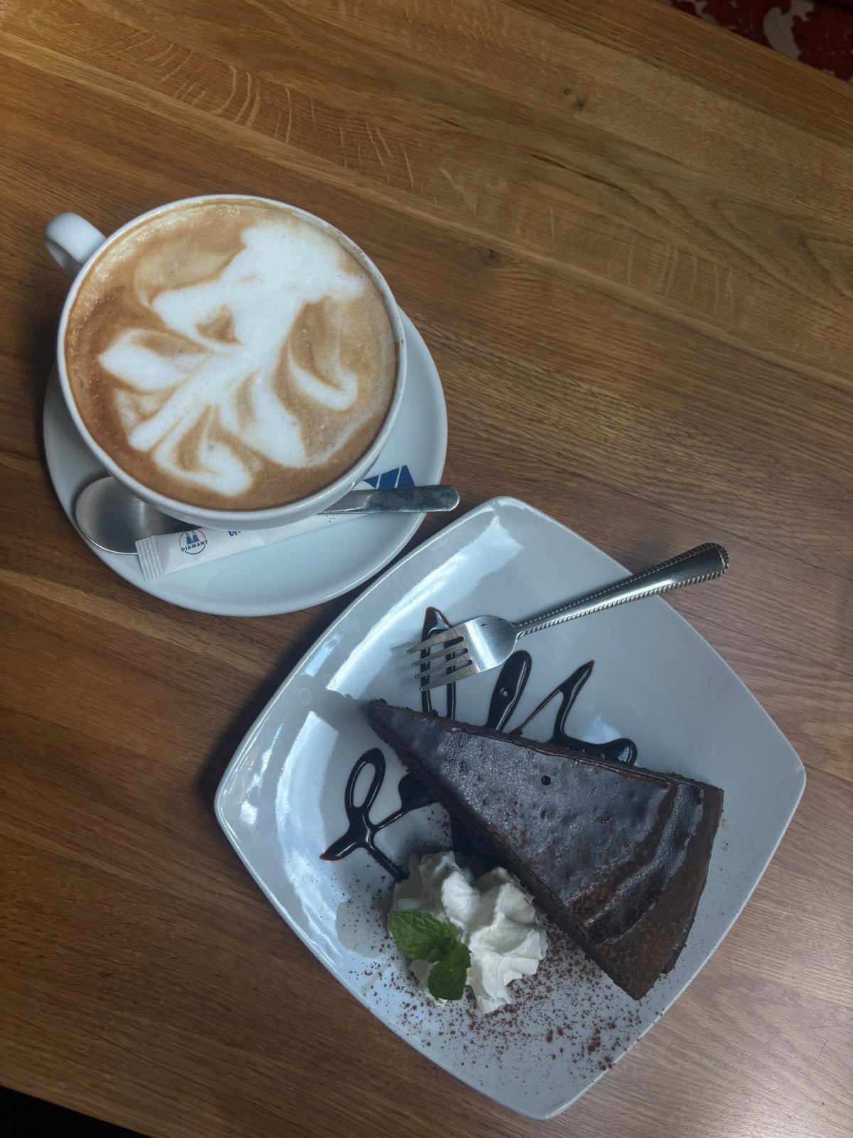 A slice of flourless chocolate cake with cream and mint, beside a cappuccino with latte art