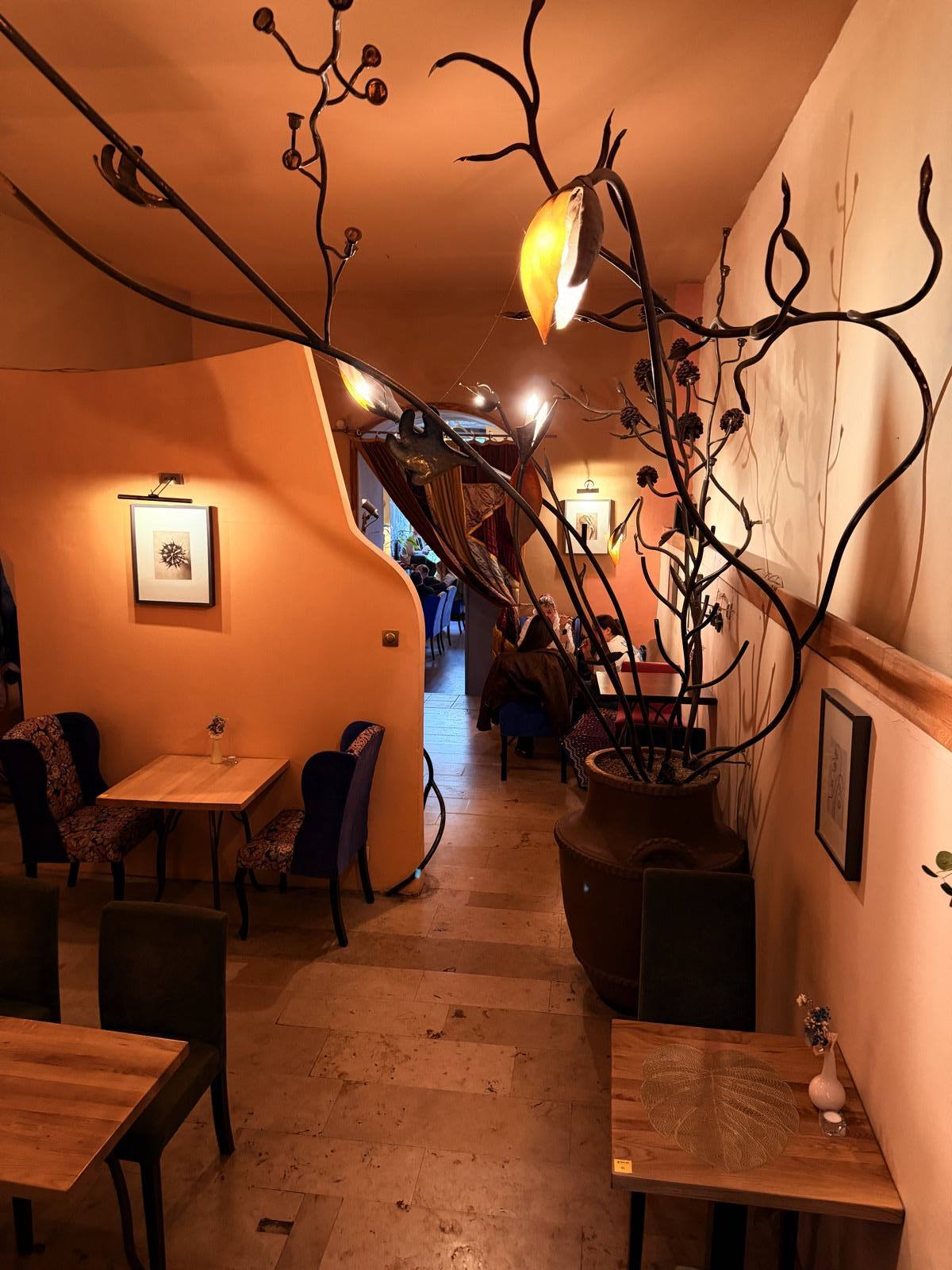 The corridor room — warm terracotta walls, hand-forged iron branches with amber leaf-lanterns overhead, blue and green armchairs and framed prints